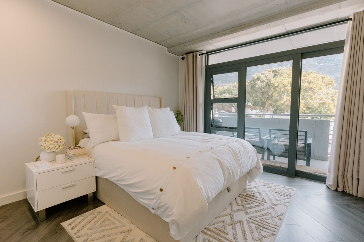 Modern bedroom featuring an exposed concrete ceiling, dark wood-look flooring, and large sliding glass doors opening onto a private balcony.