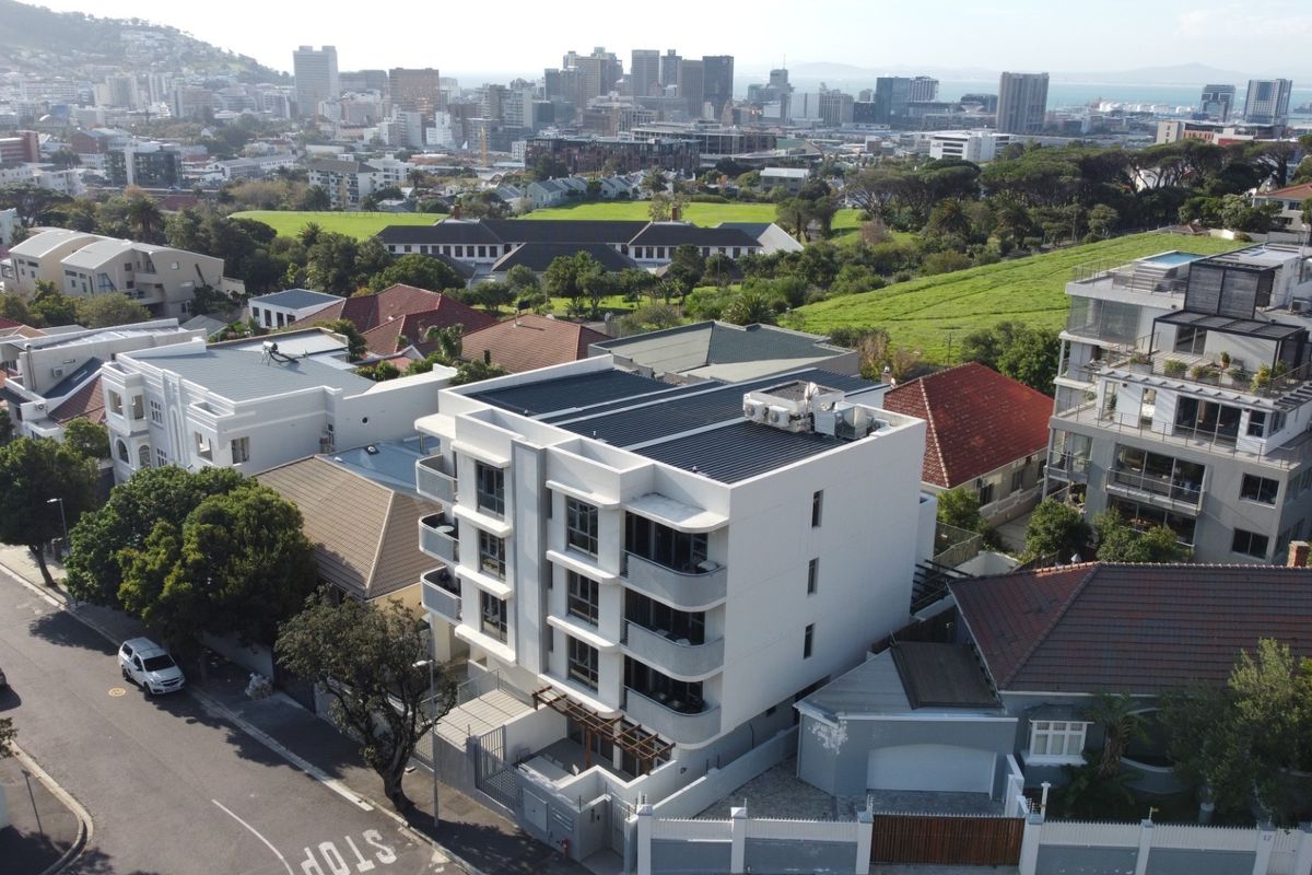 Aerial view of a modern multi-story apartment building situated in an urban neighborhood with surrounding residential properties and city skyline views.