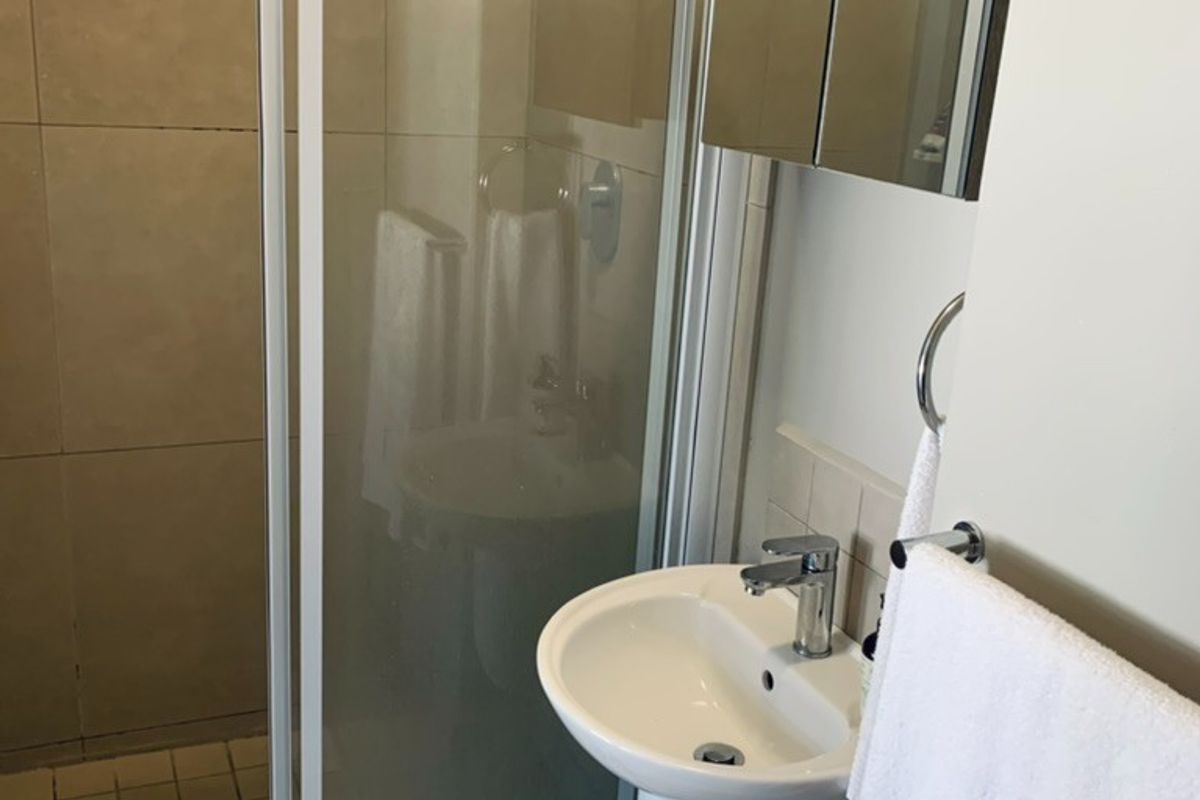 A compact bathroom featuring a glass-enclosed shower, a wall-mounted pedestal basin, and a mirrored medicine cabinet.