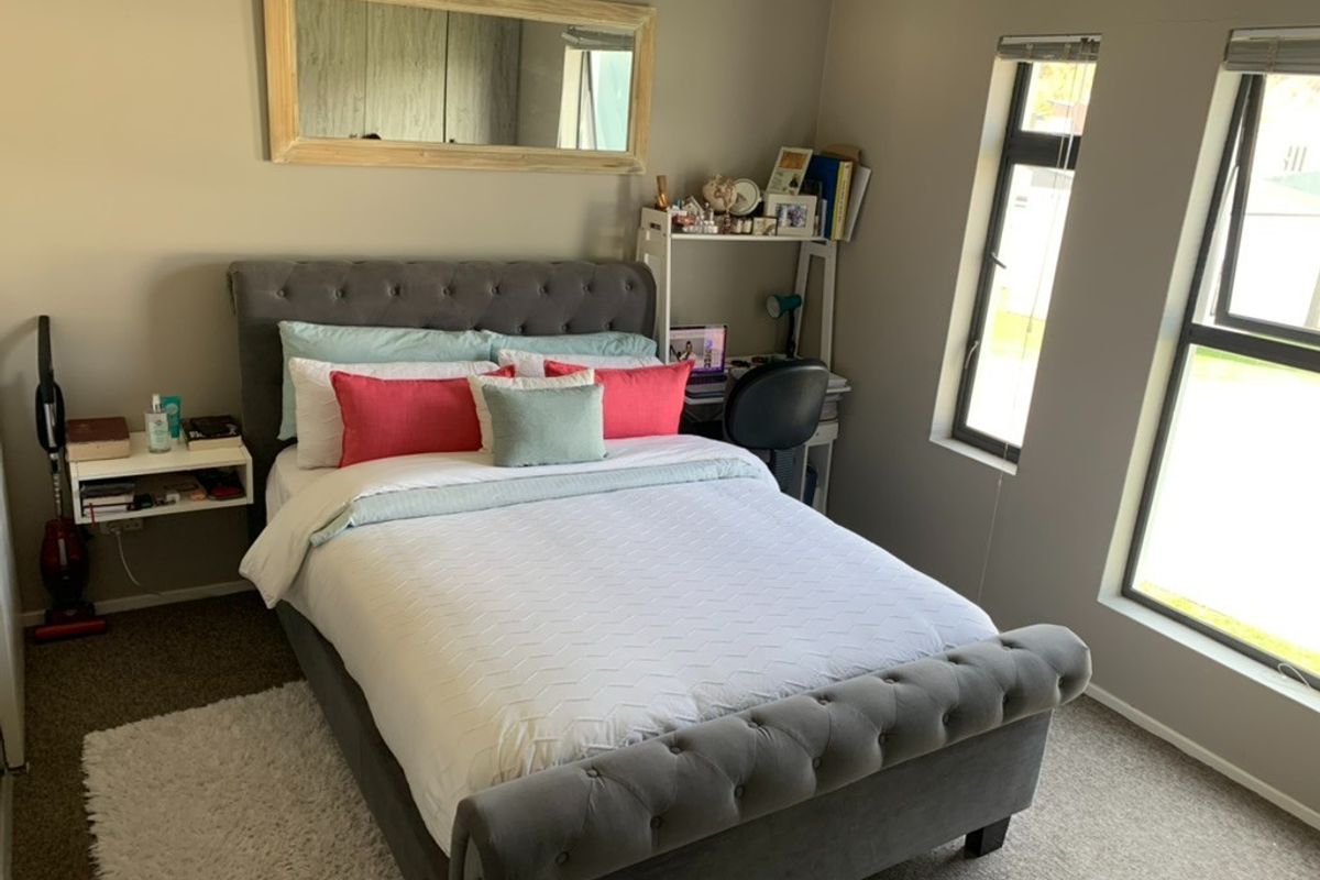 A well-lit bedroom featuring neutral wall tones, carpeted flooring, and large windows that provide natural light.