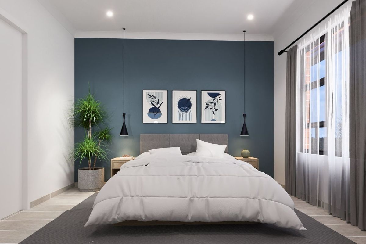 A modern, well-lit bedroom featuring a striking dark blue accent wall, recessed downlighting, and large windows with neutral curtains.