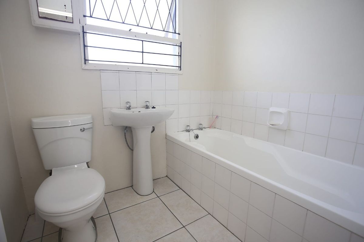 A functional bathroom featuring a white pedestal basin, standard bathtub with tiled surround, and a toilet, finished with neutral wall and floor tiles.