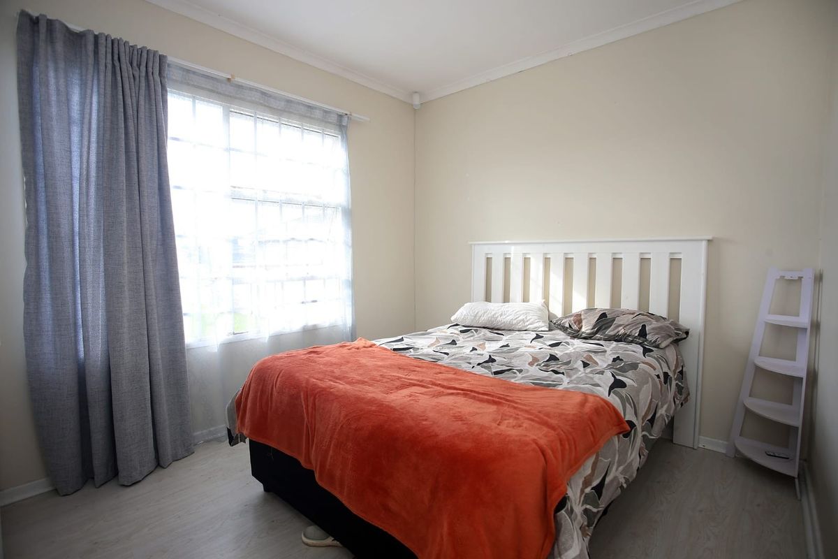 A bright bedroom featuring light-toned laminate flooring, neutral wall finishes, and a large window with curtain tracks.