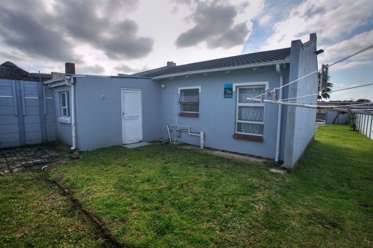 Rear view of the property featuring a small lawn, exterior wall with exposed plumbing, and a rear access door.