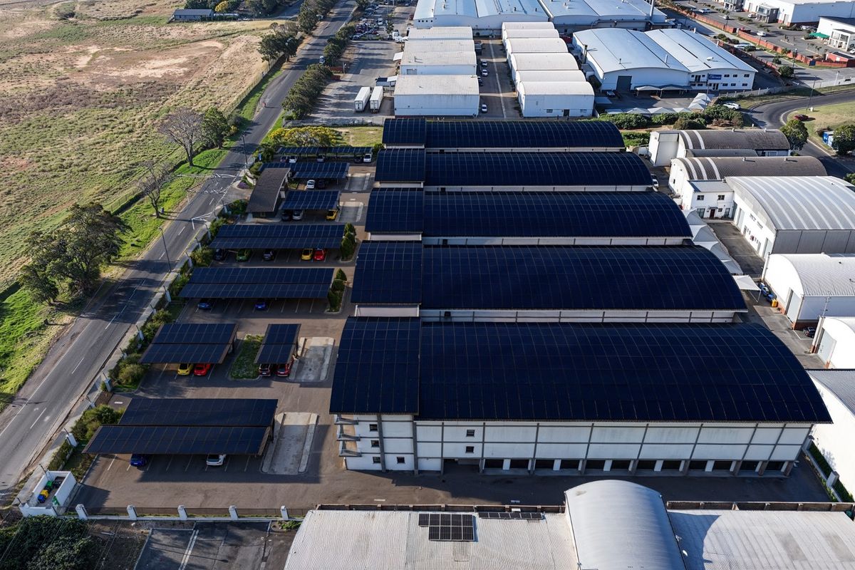 Aerial view of a commercial warehouse facility featuring extensive rooftop solar panel installations and covered parking bays.