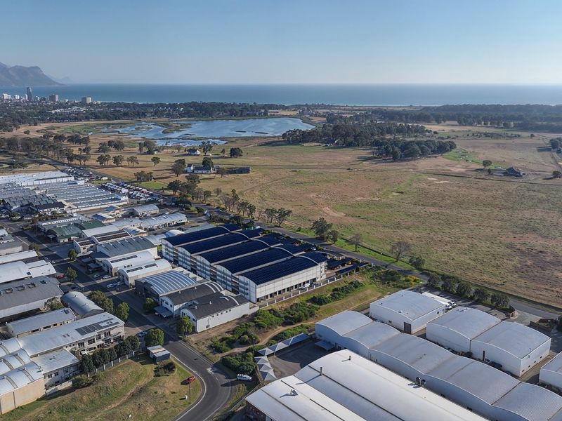 Aerial view of a commercial industrial park featuring multiple warehouse buildings with solar panel installations, situated near a coastal landscape.