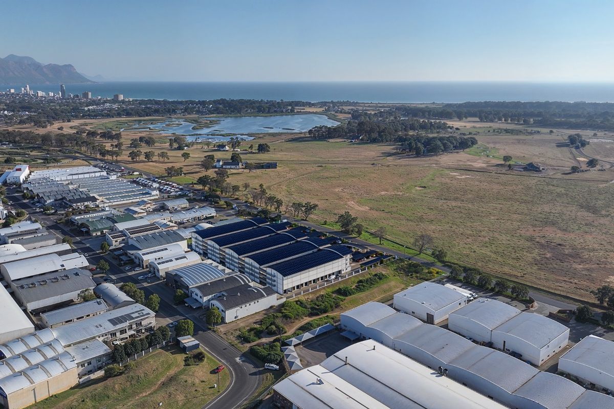 Aerial view of a commercial industrial park featuring multiple warehouse buildings with solar panel installations, situated near a coastal landscape.