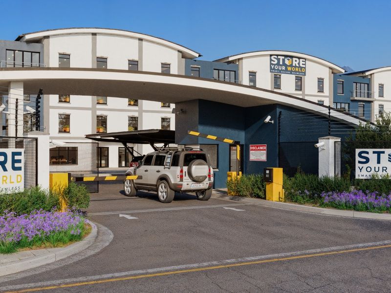 A secure commercial facility entrance featuring a modern arched gate structure, automated boom barrier, and professional signage for Store Your World.
