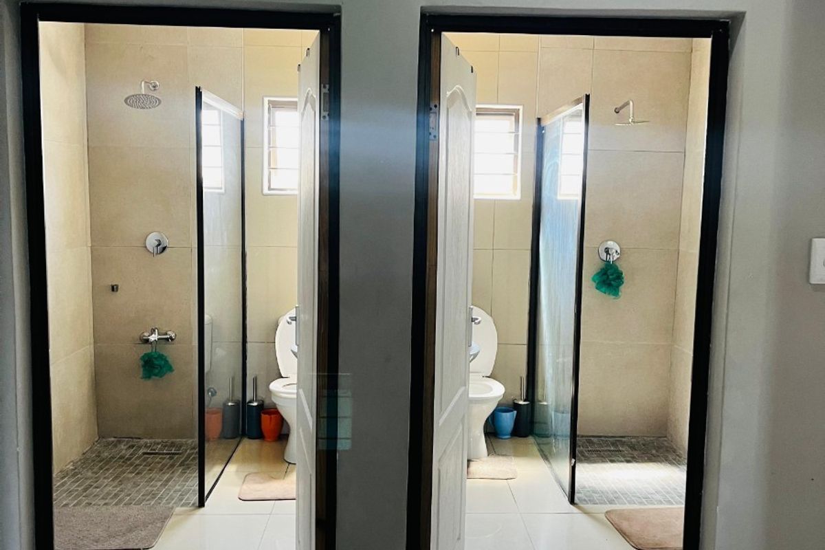 Two identical side-by-side bathrooms featuring walk-in showers with glass screens, wall-mounted shower heads, and toilets with tiled flooring and wall finishes.
