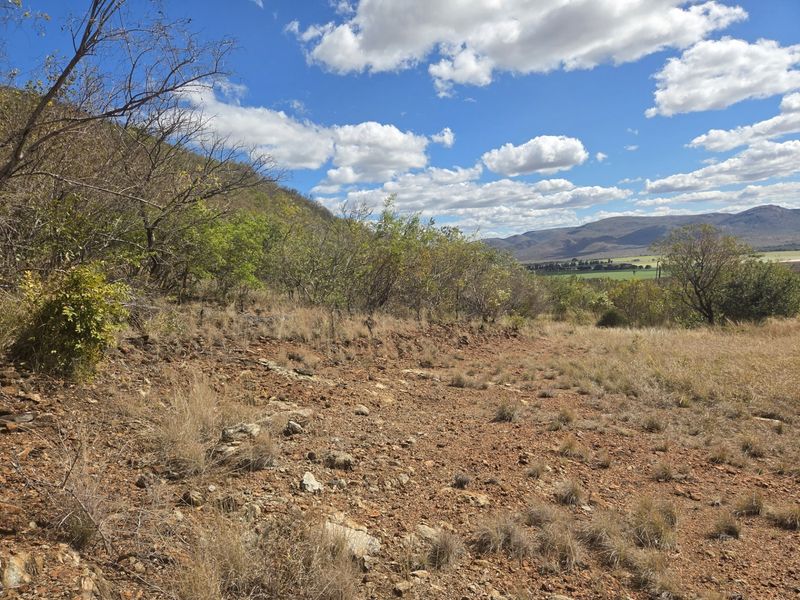 A scenic view of the natural landscape featuring sloped, rocky terrain and distant mountain ranges under a clear blue sky.