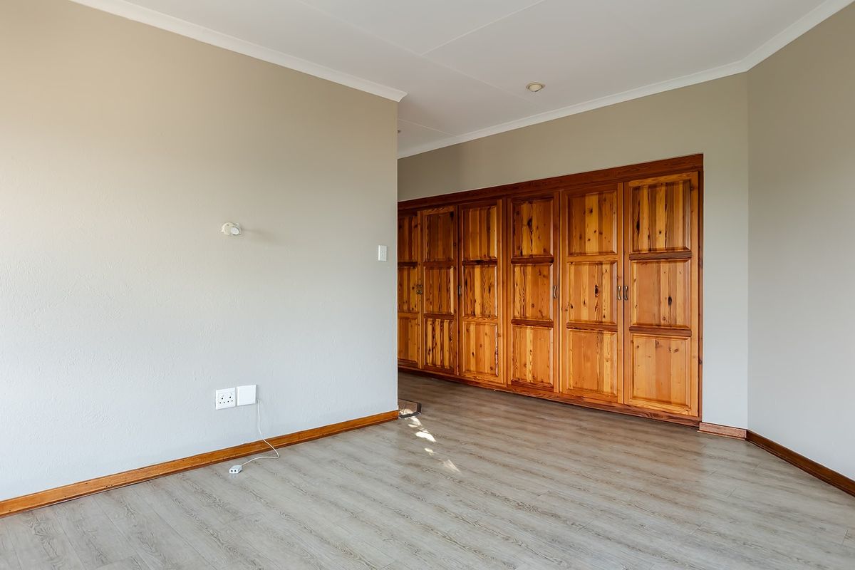 A bedroom featuring light-toned laminate flooring and extensive built-in wooden cabinetry with classic panel detailing.