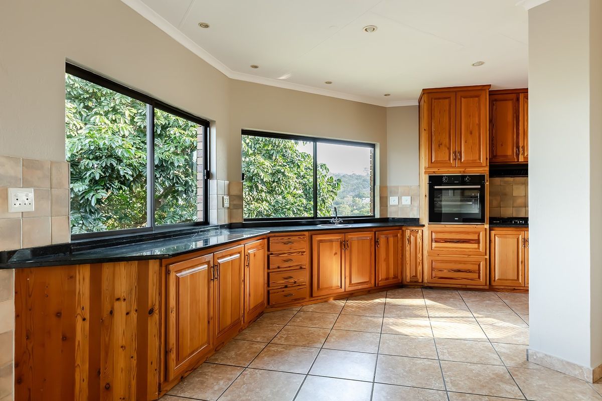 Spacious kitchen featuring natural wood cabinetry, black granite countertops, built-in oven, and large windows providing ample natural light and garden views.