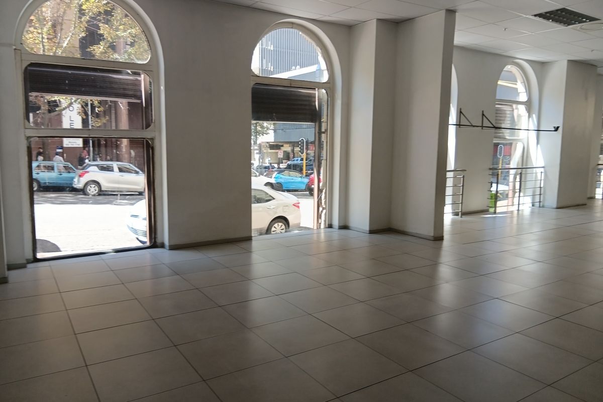Spacious retail interior featuring large arched windows, tiled flooring, and a suspended ceiling, offering excellent natural light and street-level visibility.