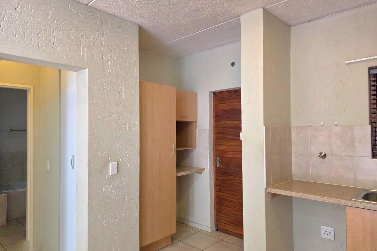 A functional kitchen area featuring built-in cabinetry, tiled splashbacks, and tiled flooring, with an adjacent doorway leading to a bathroom.