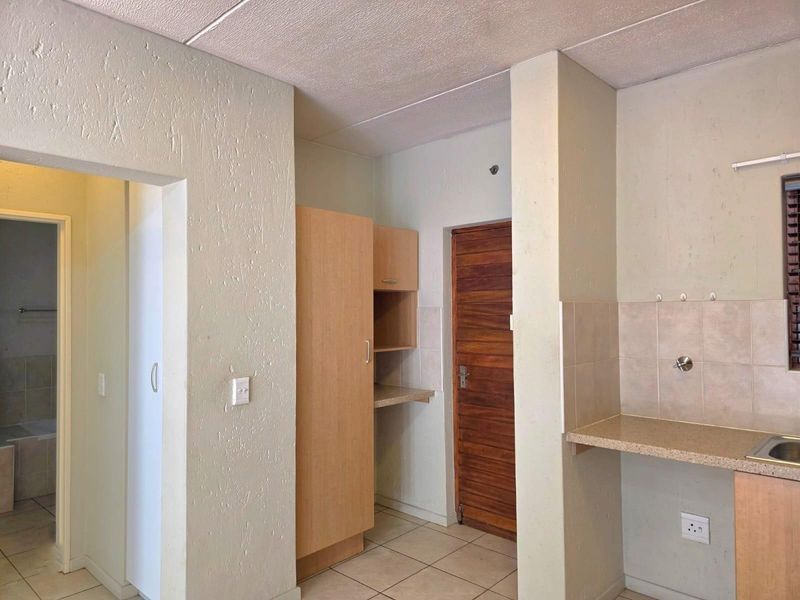 A functional kitchen area featuring built-in cabinetry, tiled splashbacks, and tiled flooring, with an adjacent doorway leading to a bathroom.