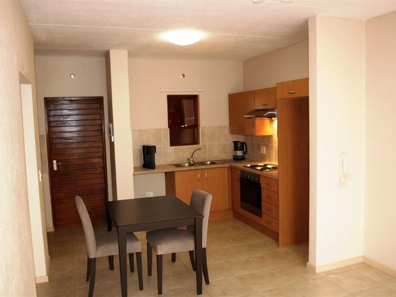Compact open-plan kitchen featuring wooden cabinetry, built-in oven, hob, extractor fan, and tiled flooring, seamlessly integrated with a dining area.