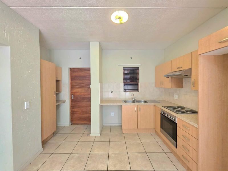 A functional kitchen featuring light wood-tone cabinetry, a built-in oven with electric hob, stainless steel sink, and tiled flooring throughout.