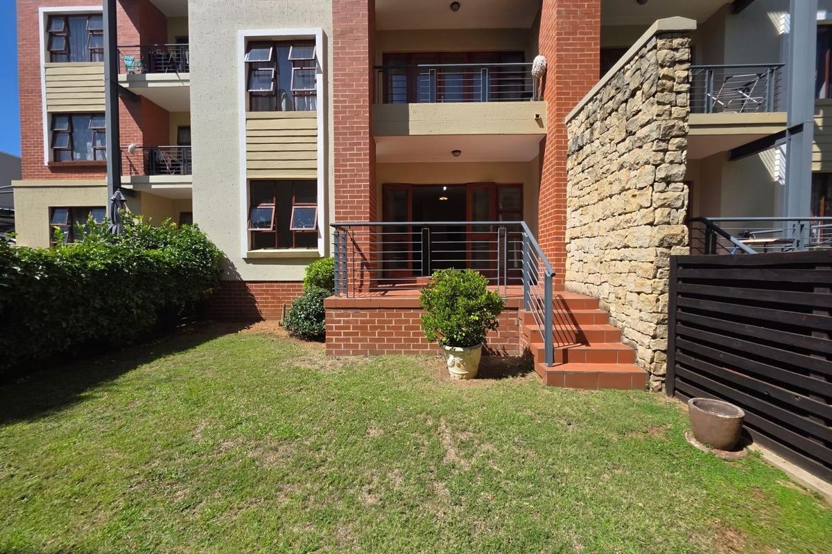 Ground floor apartment exterior featuring a private patio with brick steps, metal railings, and a small landscaped garden area.