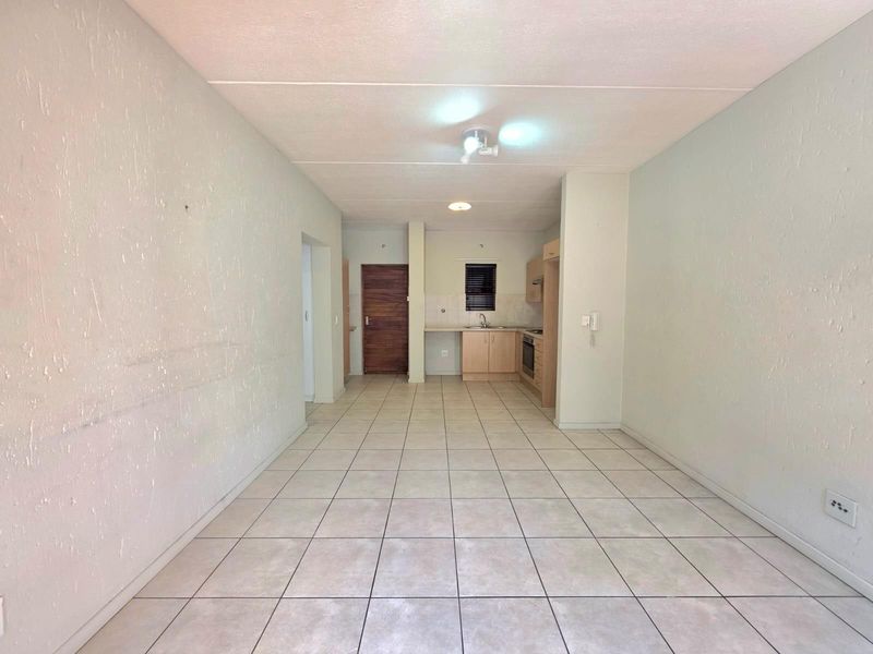 An open-plan living and kitchen area featuring tiled flooring, built-in kitchen cabinetry, and a functional layout suitable for modern apartment living.