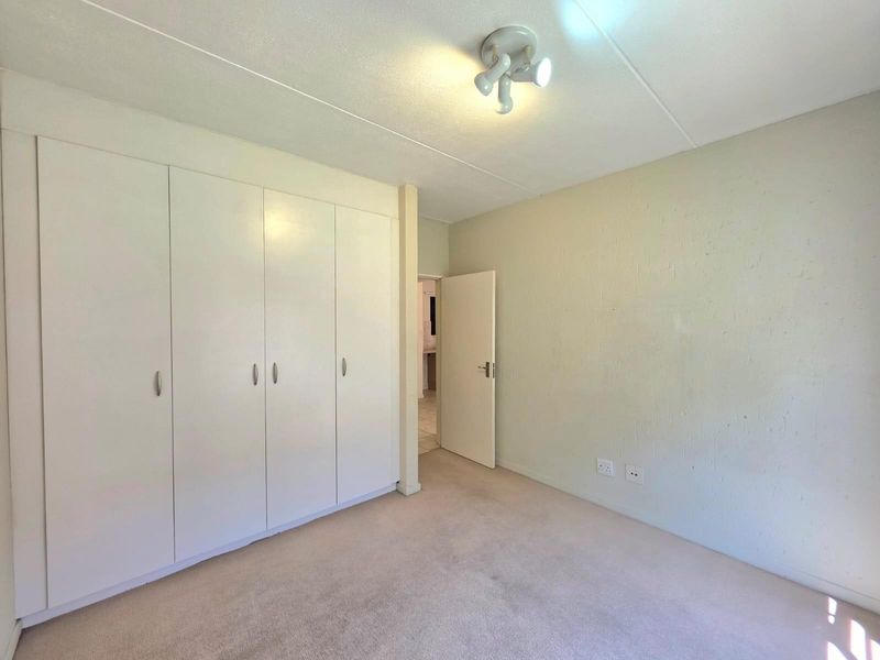 A bright, empty bedroom featuring built-in floor-to-ceiling wardrobes, neutral carpeting, and a central ceiling light fixture.