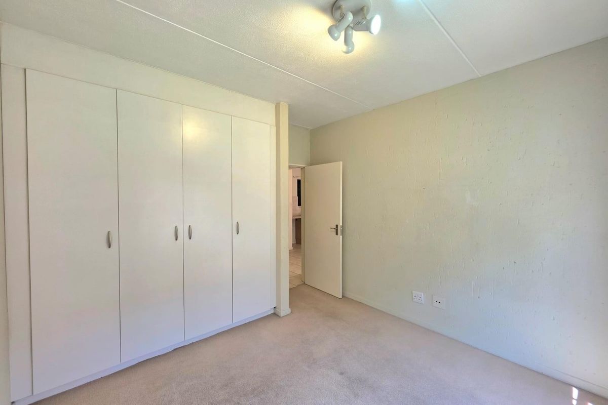 A bright, empty bedroom featuring built-in floor-to-ceiling wardrobes, neutral carpeting, and a central ceiling light fixture.