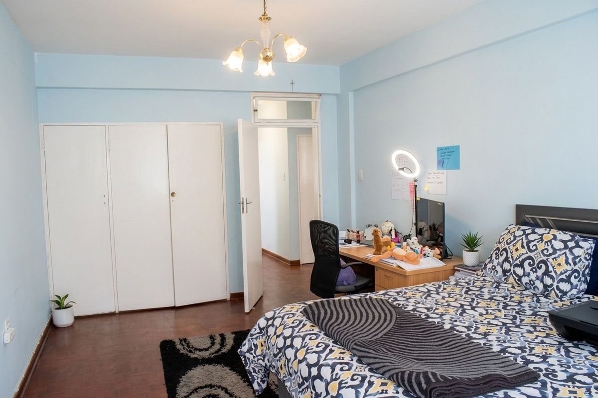 A bedroom featuring built-in cupboards, wooden flooring, and a ceiling light fixture, providing a functional living space.