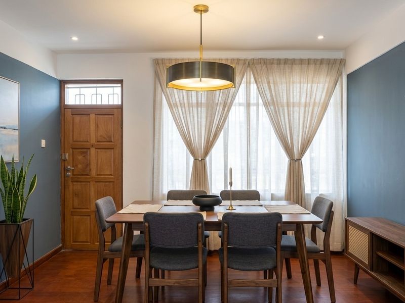 A well-presented dining room featuring warm timber flooring, a classic wooden door with transom window, and elegant pendant lighting.