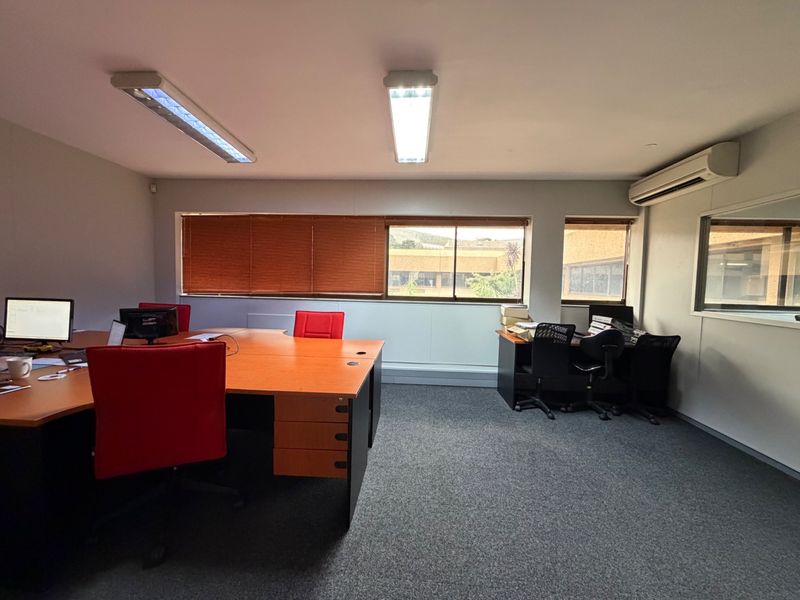 A functional office space featuring carpeted flooring, split-system air conditioning, and large windows with venetian blinds, providing a practical work environment.