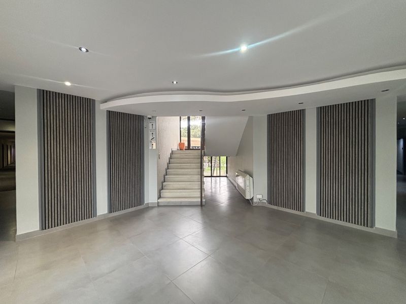 Modern office building entrance lobby featuring contemporary slatted timber wall paneling, tiled flooring, and a distinctive curved bulkhead ceiling design.