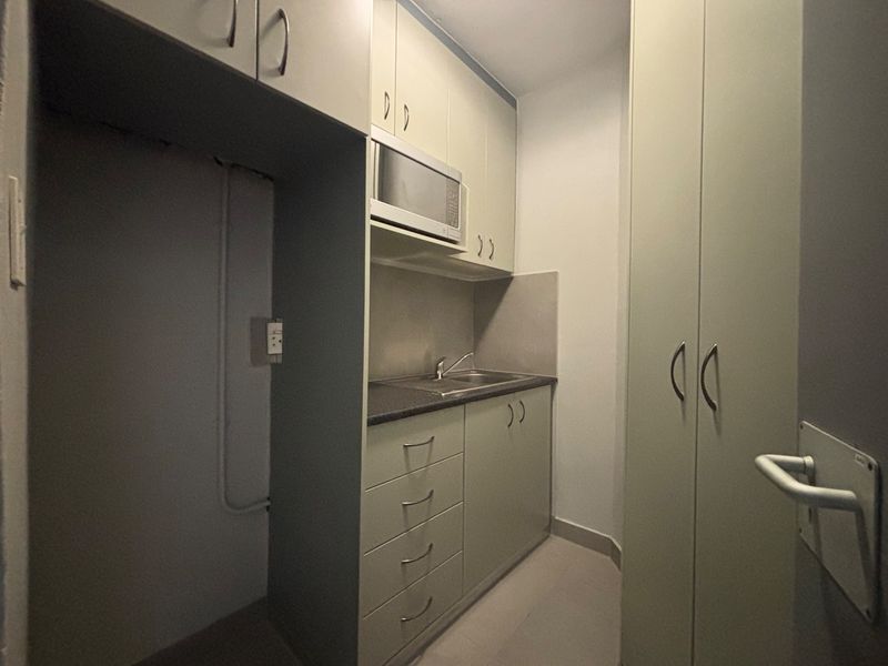 A compact kitchenette featuring built-in cabinetry, a stainless steel sink, integrated microwave, and additional full-height storage cupboards.