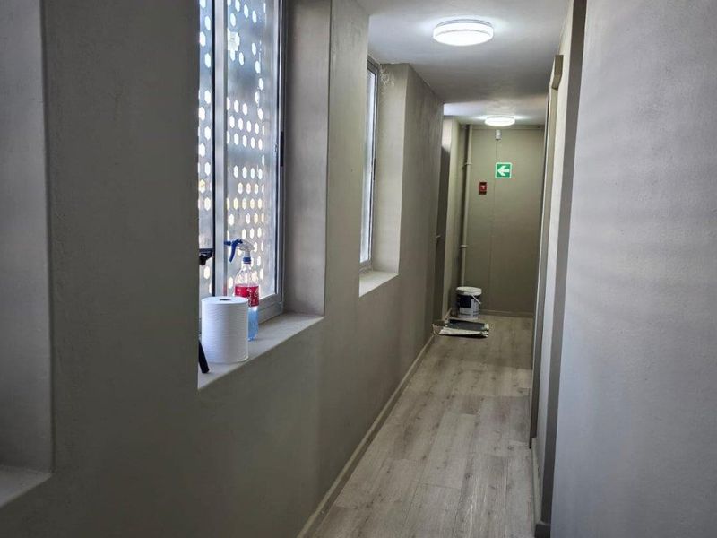 A clean, well-lit commercial hallway featuring modern wood-look flooring, neutral wall finishes, and recessed ceiling lighting.
