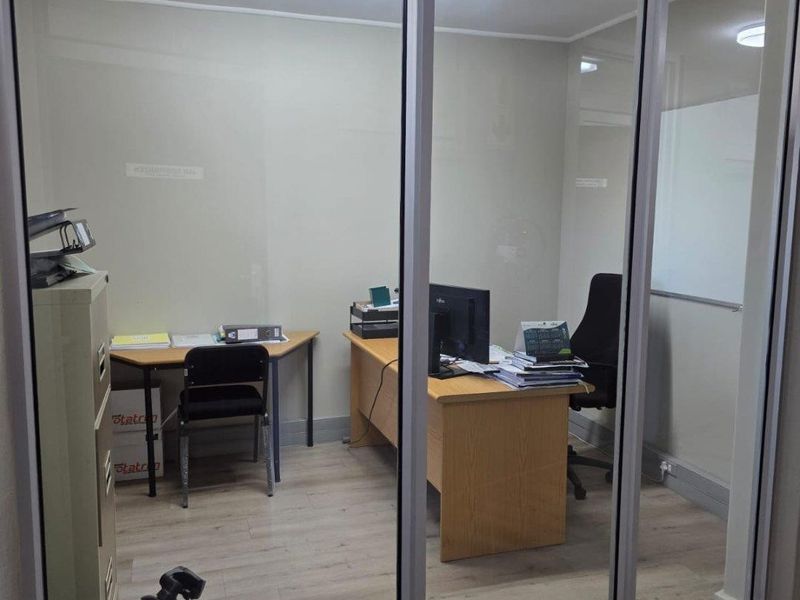 A functional commercial office space featuring glass partitioning, wood-look flooring, and integrated fluorescent lighting.