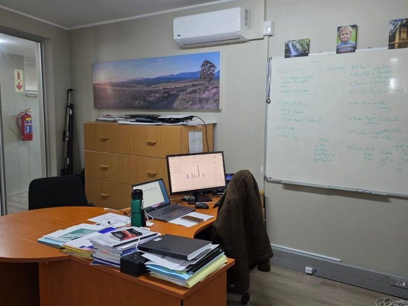 A functional commercial office space featuring a wall-mounted air conditioning unit, fluorescent lighting, and a whiteboard.