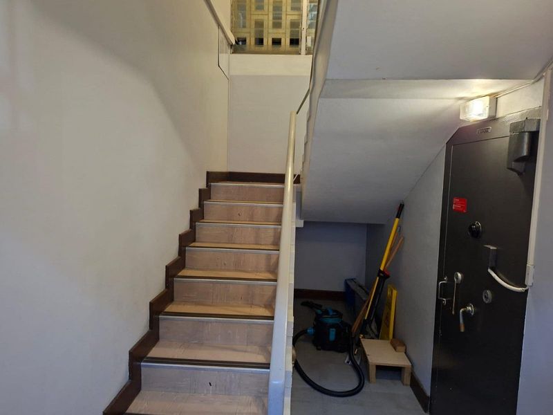 A functional interior stairwell featuring a metal handrail, tiled stair treads, and a secure heavy-duty metal door at the base.
