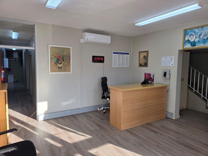 A commercial reception area featuring wood-look flooring, a built-in reception desk, wall-mounted air conditioning unit, and fluorescent lighting.