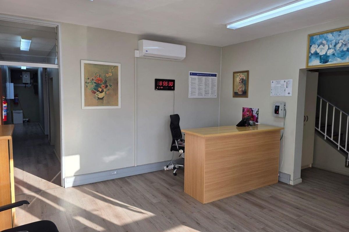 A commercial reception area featuring wood-look flooring, a built-in reception desk, wall-mounted air conditioning unit, and fluorescent lighting.