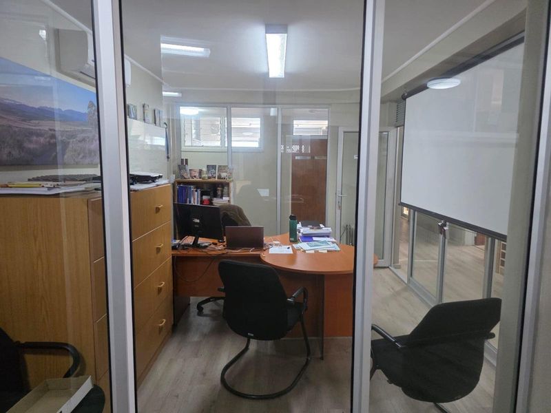 A functional office space featuring glass partitioning, laminate flooring, and a built-in projection screen, suitable for professional use.