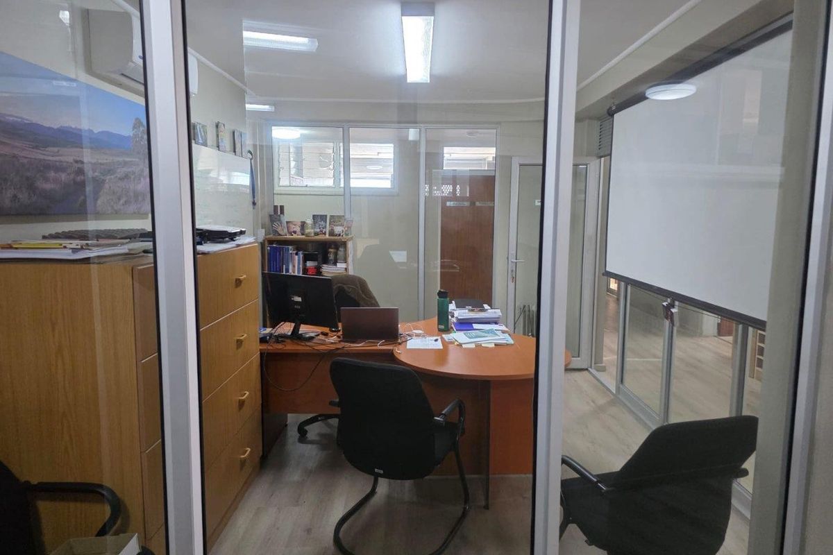 A functional office space featuring glass partitioning, laminate flooring, and a built-in projection screen, suitable for professional use.
