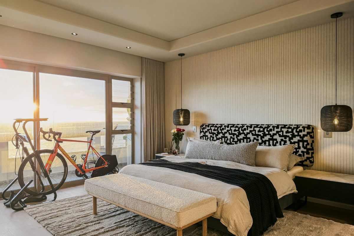 A modern, well-appointed bedroom featuring recessed ceiling lighting, textured wall paneling, and large sliding glass doors leading to a balcony with scenic views.