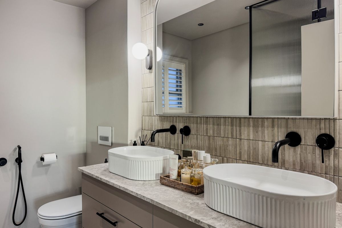Modern bathroom featuring a double vanity with fluted vessel sinks, wall-mounted matte black faucets, stone countertop, and a large arched mirror.