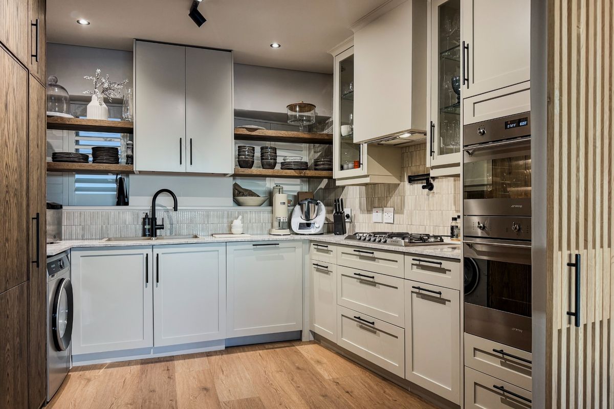 Modern kitchen featuring light cabinetry, integrated oven, gas hob, timber shelving, and wood-look flooring, offering a clean and functional culinary space.