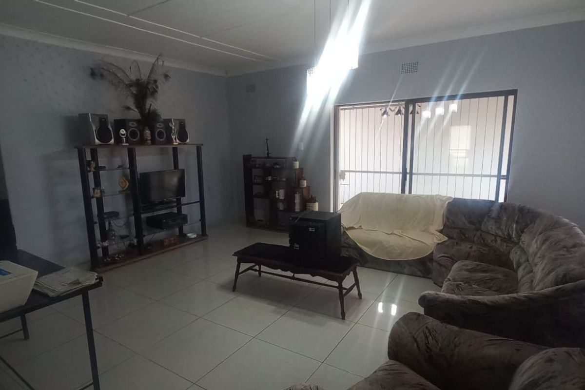 A spacious living room featuring tiled flooring, large windows with blinds, and sliding glass doors leading to the exterior.