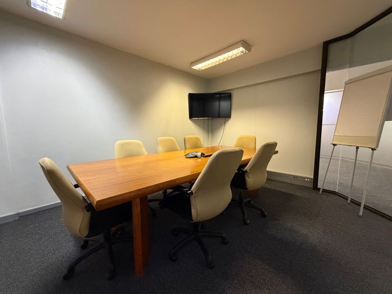 A functional office meeting room featuring carpeted flooring, fluorescent lighting, and a glass partition wall, suitable for professional collaborative work.