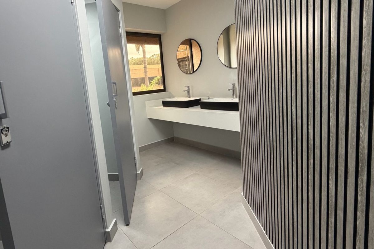 Modern office bathroom featuring a double vanity with vessel sinks, sleek wall-mounted faucets, and a contemporary slatted wood feature wall.