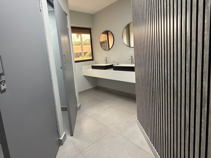 Modern office bathroom featuring a double vanity with vessel sinks, sleek wall-mounted faucets, and a contemporary slatted wood feature wall.