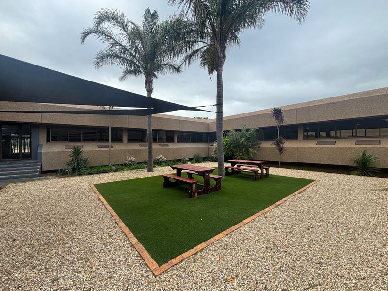 A well-maintained office courtyard featuring artificial turf, gravel landscaping, and a shade sail providing a comfortable outdoor break area.