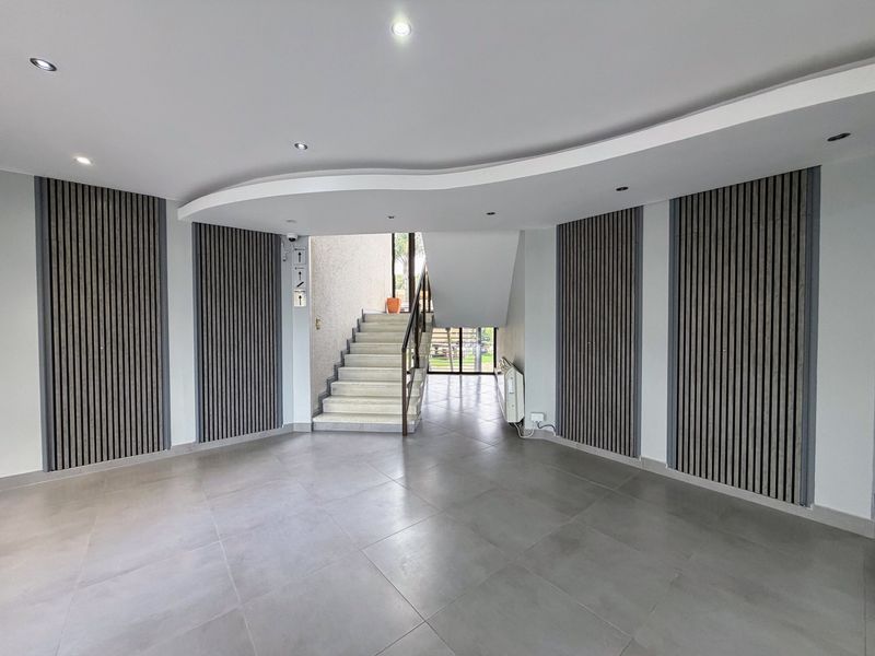 Modern office entrance foyer featuring contemporary slatted timber wall paneling, tiled flooring, and a curved bulkhead ceiling with recessed lighting.