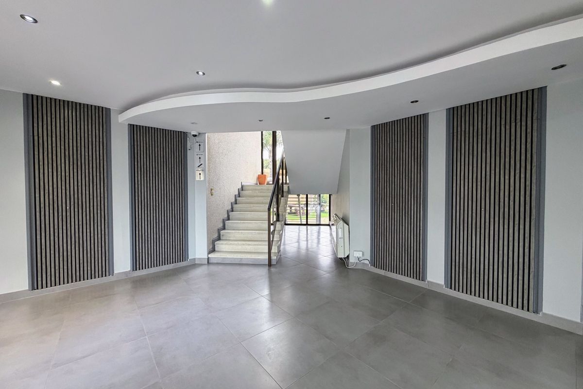 Modern office entrance foyer featuring contemporary slatted timber wall paneling, tiled flooring, and a curved bulkhead ceiling with recessed lighting.