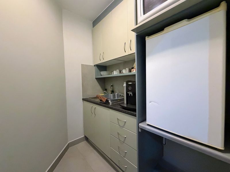 Compact office scullery area featuring built-in cabinetry, a stainless steel sink, and dedicated space for a small refrigerator and microwave.