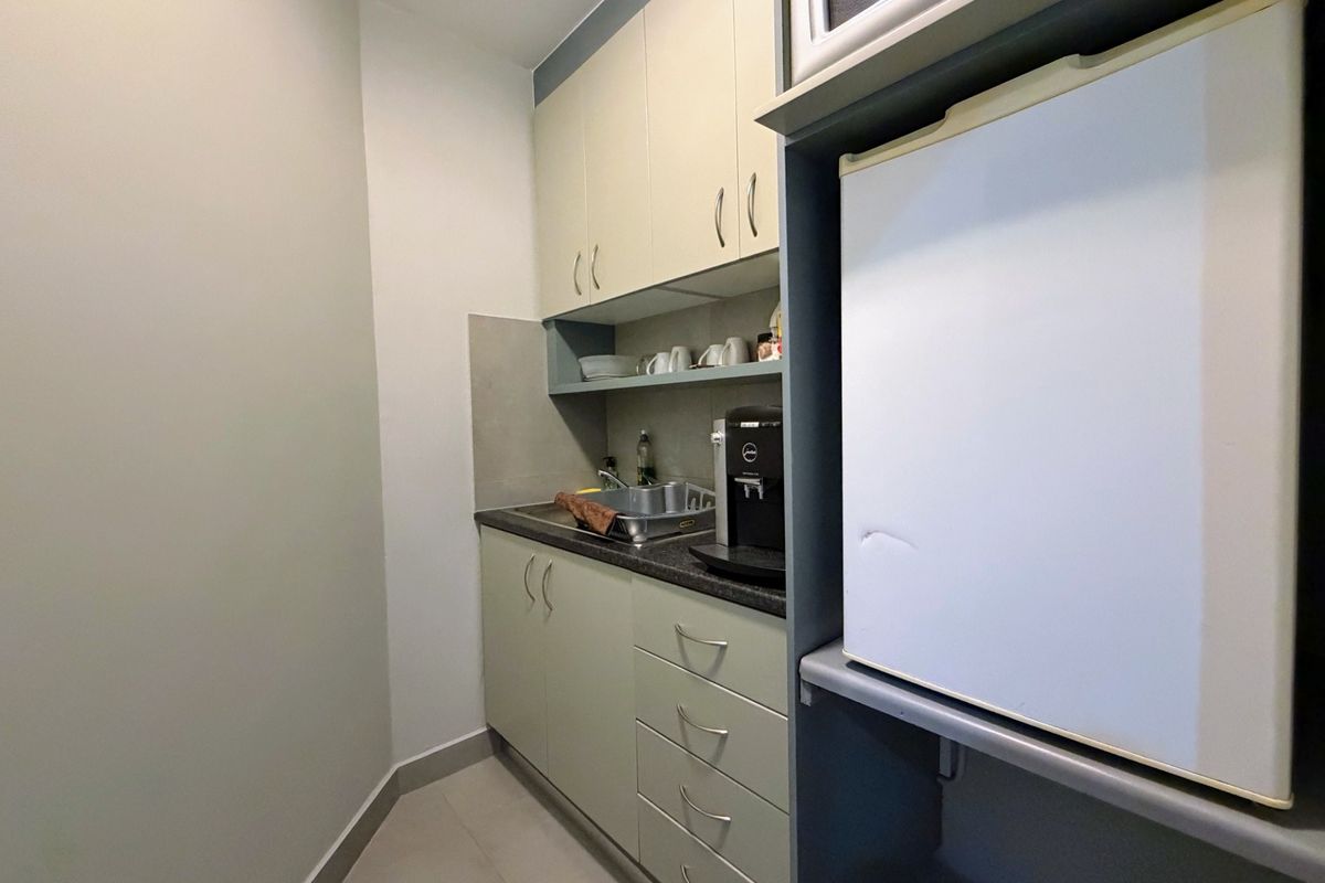 Compact office scullery area featuring built-in cabinetry, a stainless steel sink, and dedicated space for a small refrigerator and microwave.